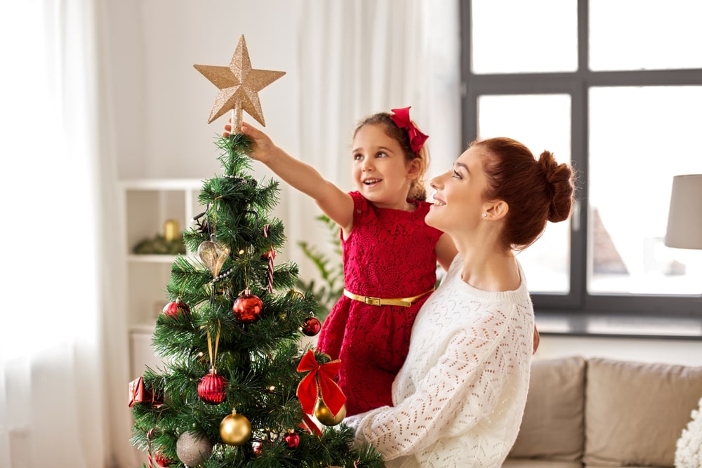 Mother and daughter placing the star topper on the Christmas tree